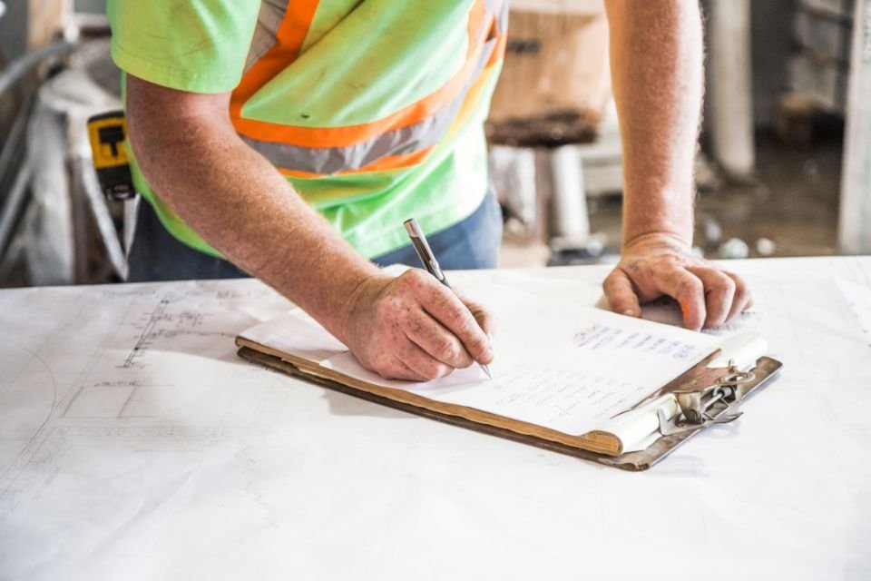 A site supervisor in a high visibility vest working through paperwork on a clipboard at a job site, the environment our collectors work in